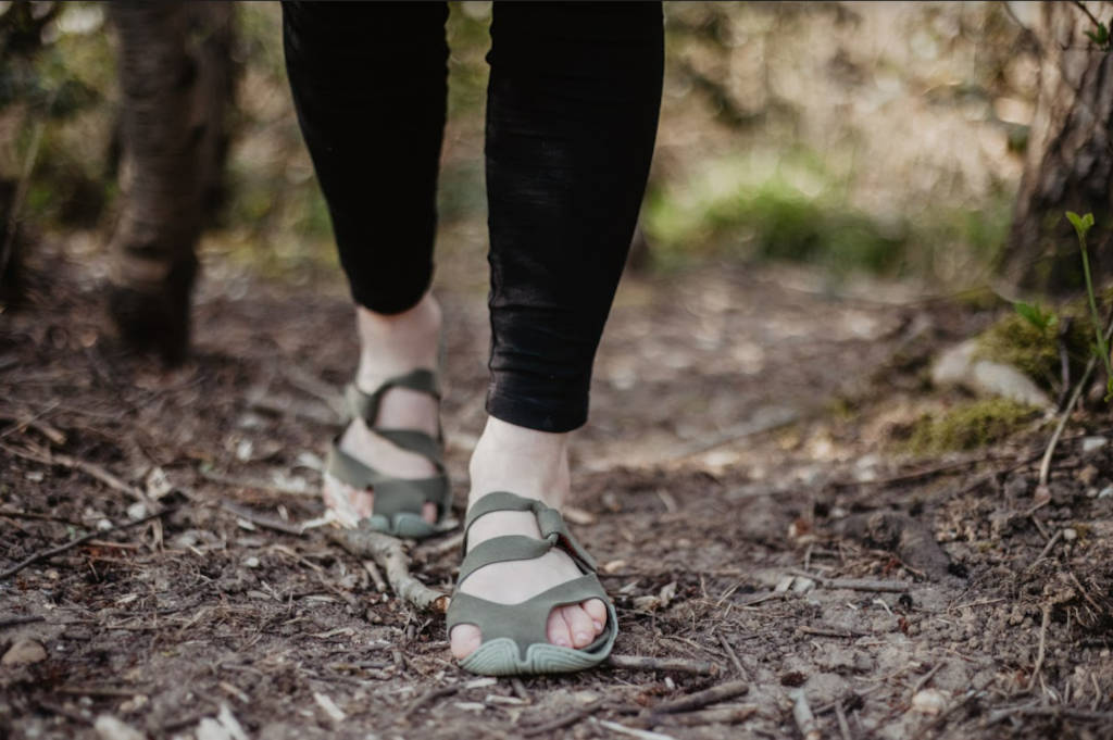 Zwei Füße, etwa bis zu den Waden im Bild, auf einem Waldweg. An den Füßen Sandalen von Wildling.