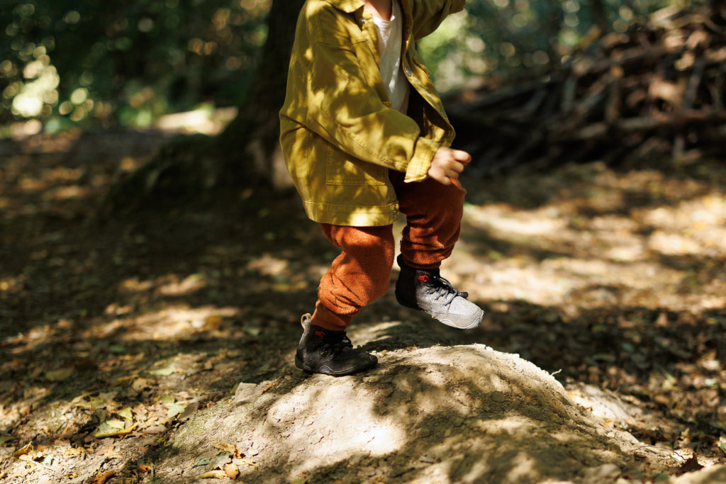 A child running in the shade of sunlit trees. They are wearing Wildling barefoot shoes on their feet. The child is in the picture up to his shoulders.