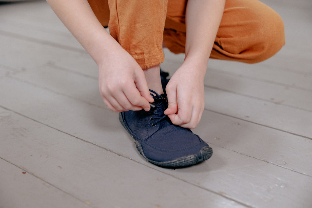 Close-up: Hands lacing up a Wildling barefoot shoe.