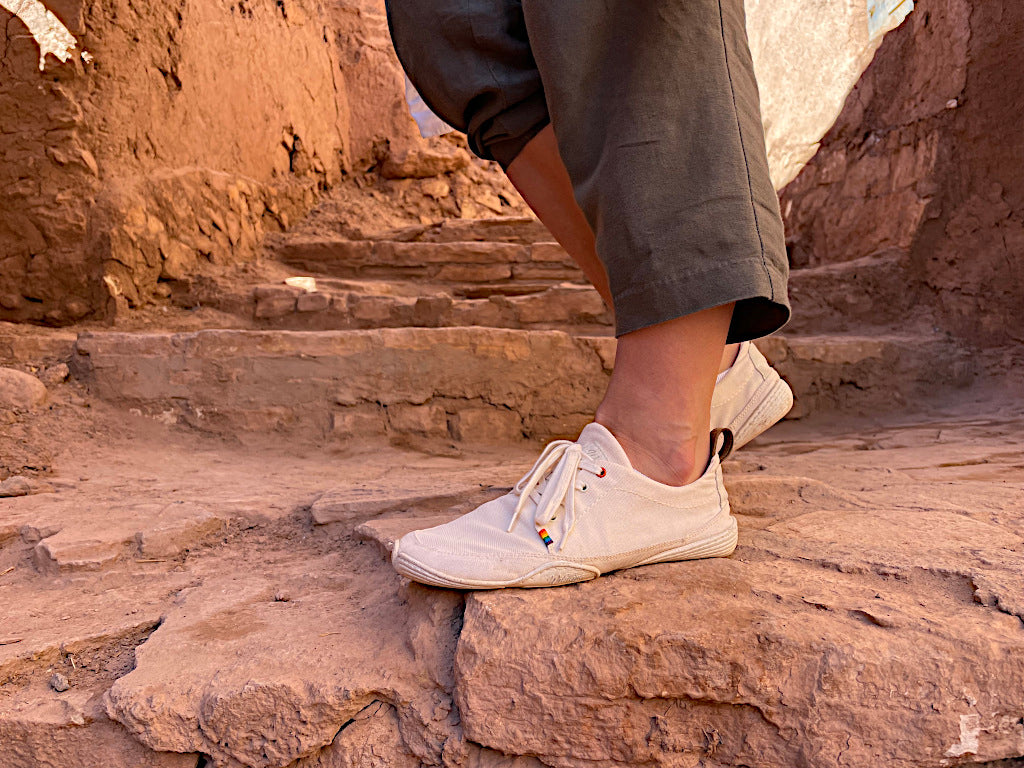 Close-up: a foot from the side in a Wildling barefoot shoe on rocky ground.