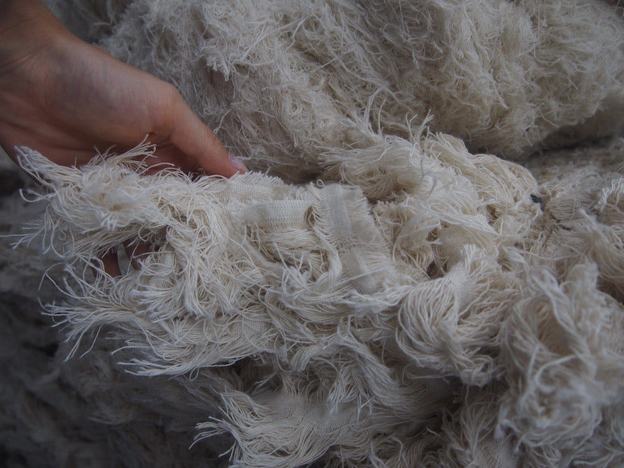 A hand reaches into a pile of textile waste.